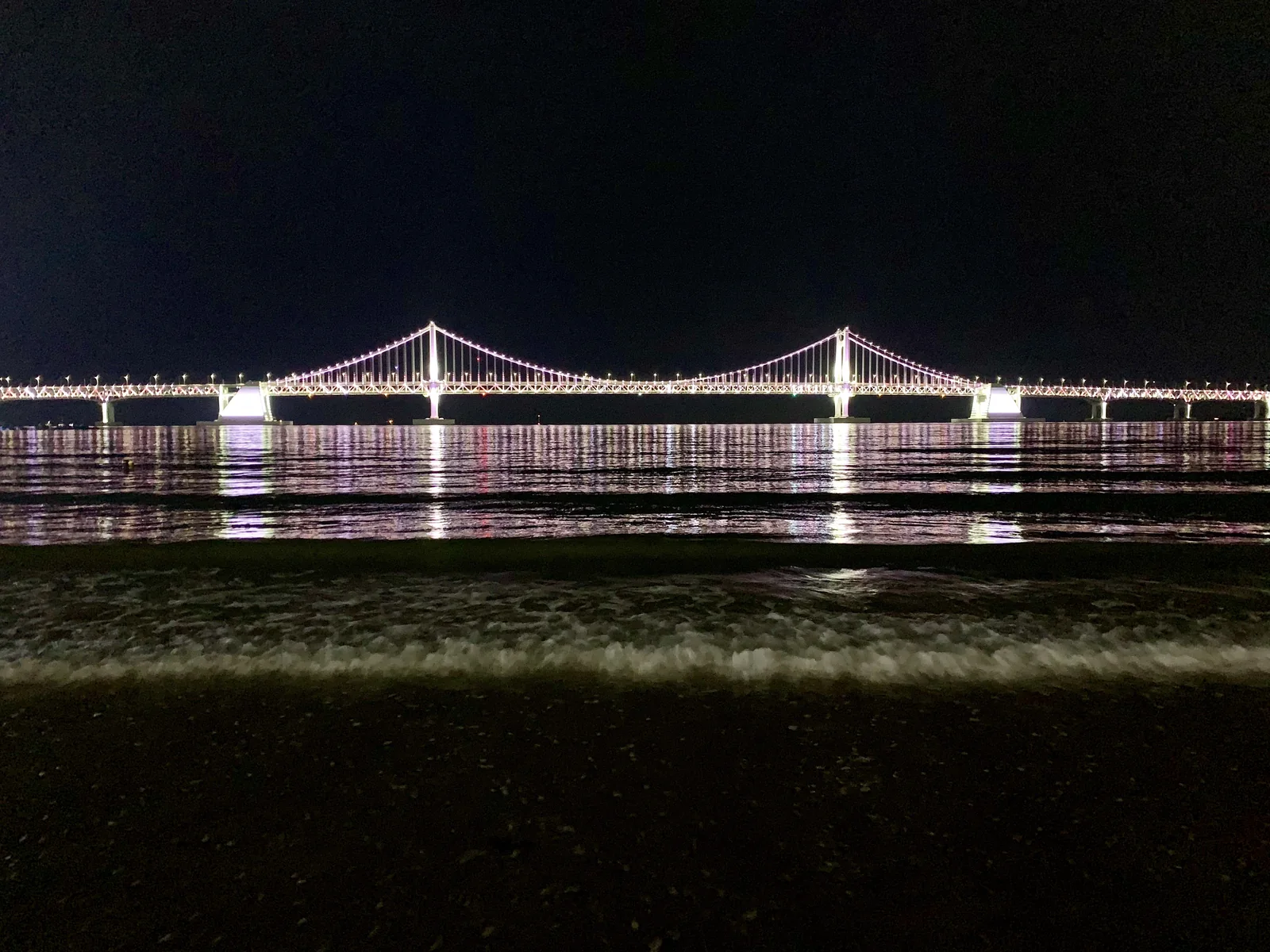 Gwangan Bridge illuminated at night above Gwangalli Beach in Busan.
