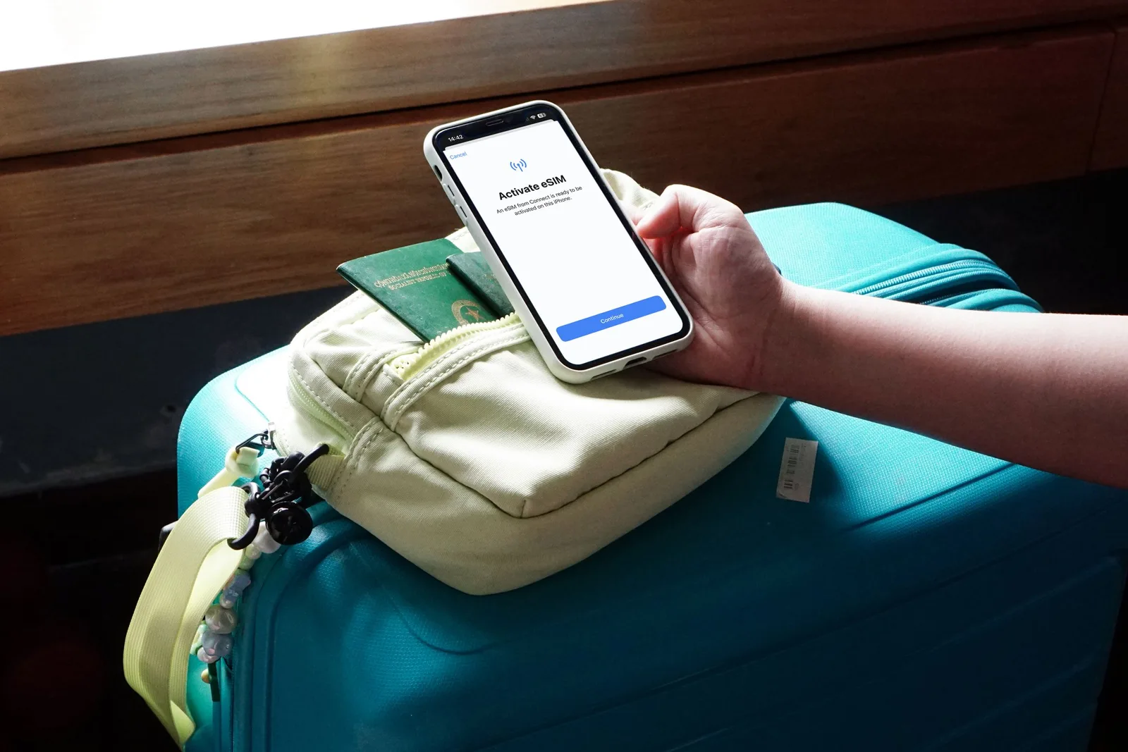 A traveler activating an eSIM on a smartphone beside a passport and suitcase