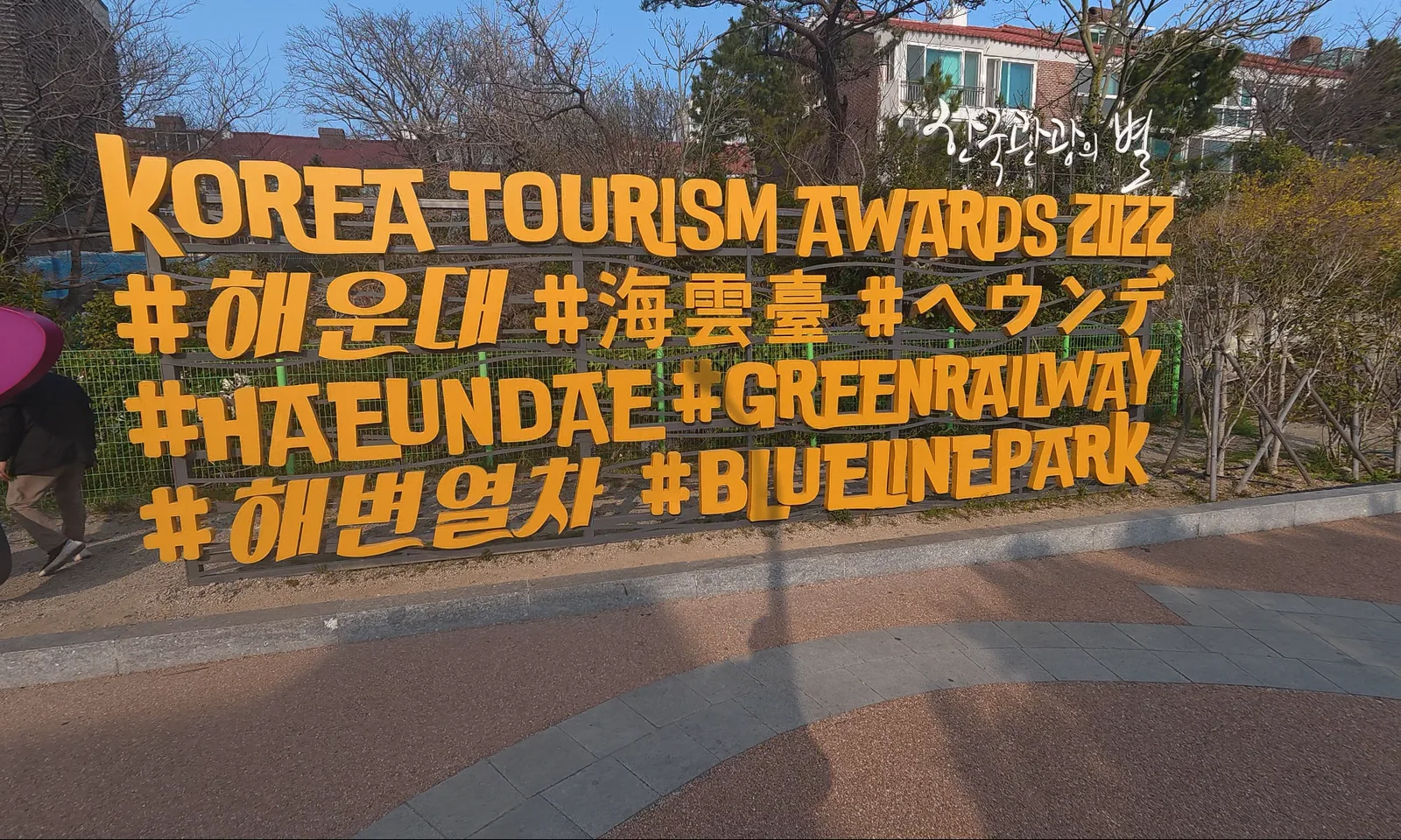 Large Haeundae Blueline Park sign with tourism hashtags near the coastal route in Busan.