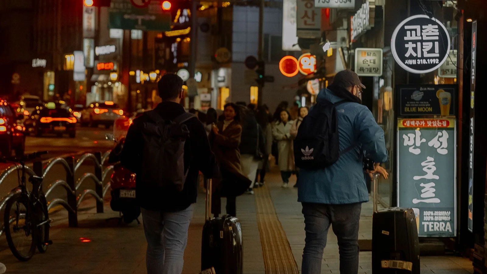Travelers pulling suitcases along a busy Korean city street at night