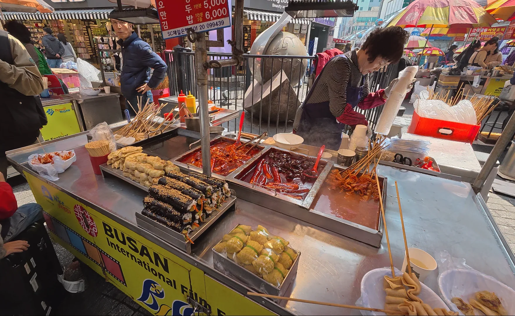 Street food stall in Nampo-dong, Busan, with kimbap, tteokbokki, eomuk, and market snacks.