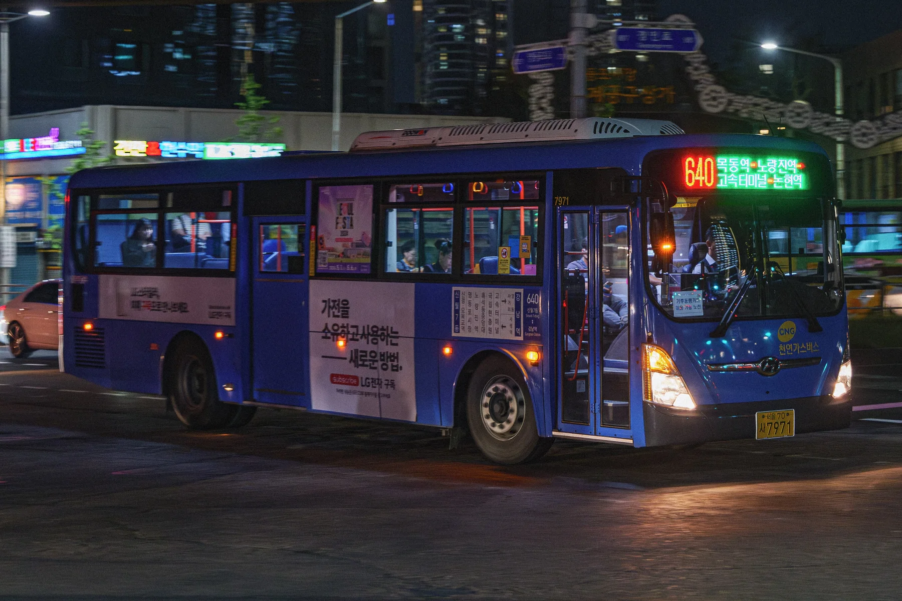 A blue Seoul city bus traveling through a brightly lit street at night