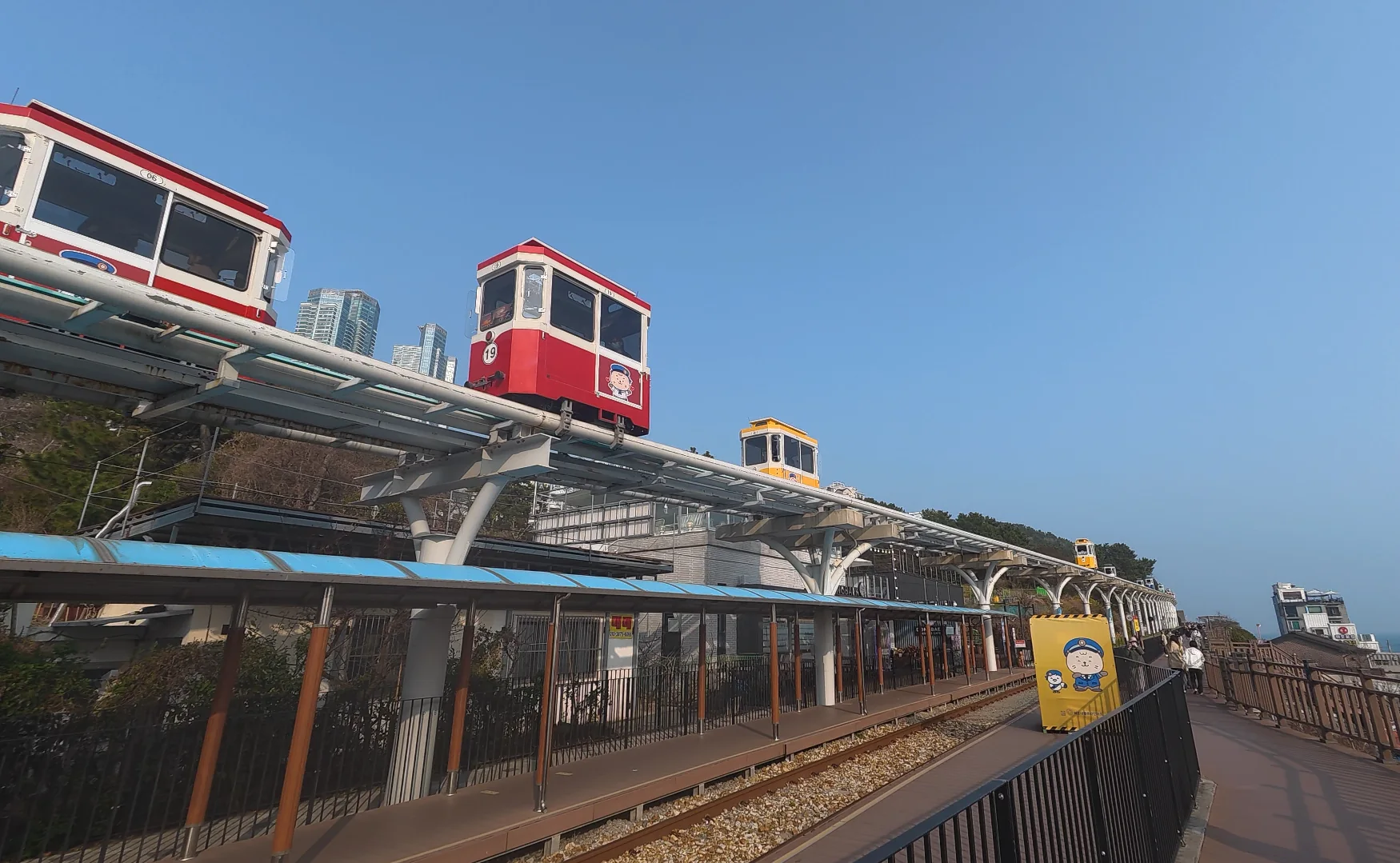Colorful Sky Capsule cars on the elevated Haeundae Blueline Park track above the coastal walkway in Busan.