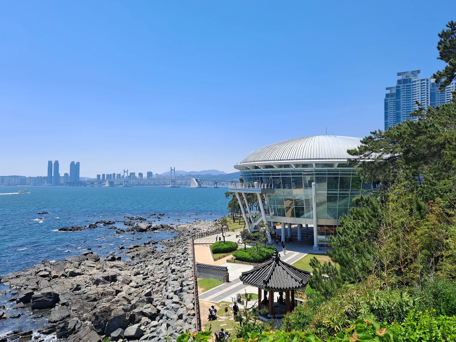 Dongbaekseom Island in Busan with Nurimaru APEC House and Gwangan Bridge visible across the water.