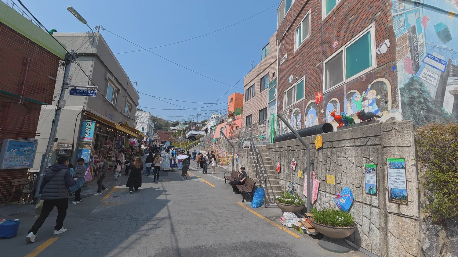 Main walking street in Gamcheon Culture Village with murals, shops, and visitors.
