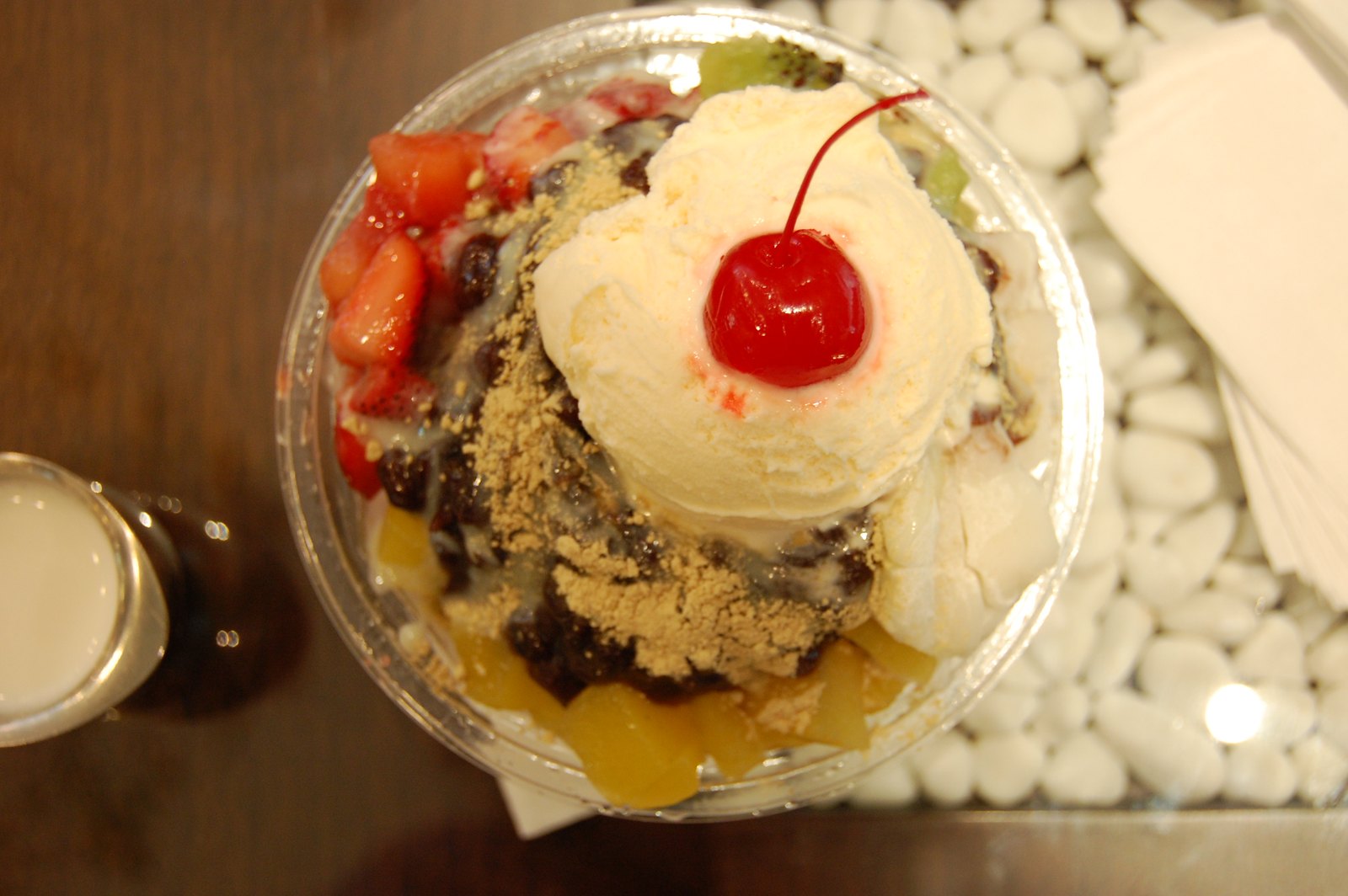 Bowl of Korean patbingsu shaved ice dessert with red beans, ice cream, fruit, and rice cake toppings