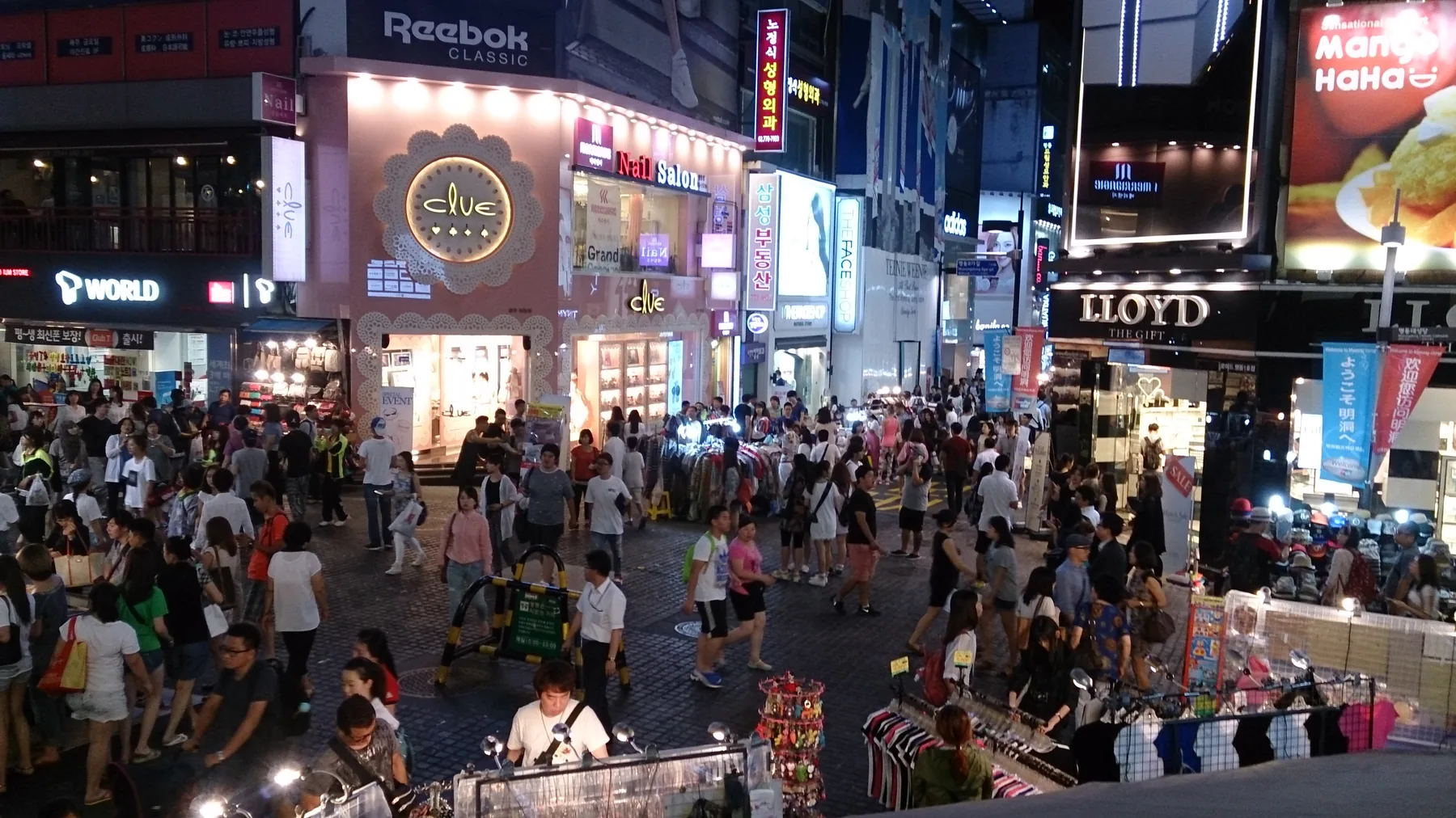 Crowded shopping street in Myeongdong, Seoul with pedestrians and storefronts.
